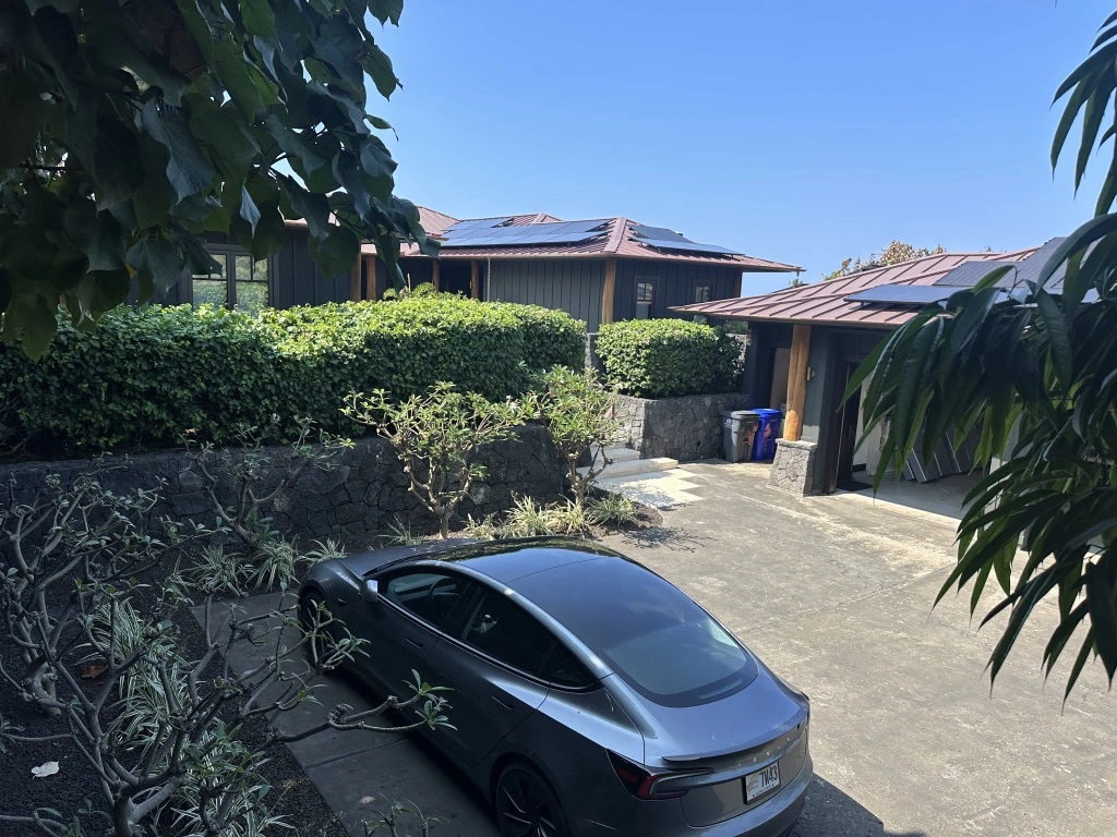 Residential property featuring rooftop solar panels and an electric car parked in the driveway, showcasing sustainable living.