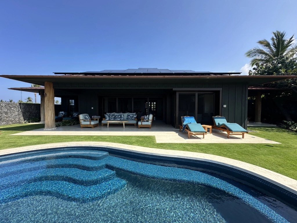 Luxury home equipped with solar panels on the roof, poolside seating area, and eco-friendly design.