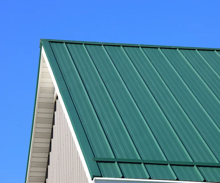 Close-up of a steep-pitched roof covered in green standing seam metal panels with white siding on the gable end.