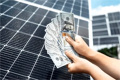 A person holding a fan of hundred-dollar bills in front of solar panels, illustrating energy savings in Hawaii.