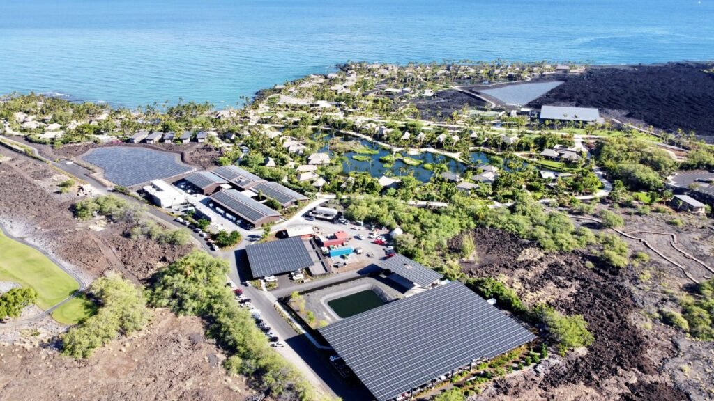 Aerial view of a large commercial solar array on volcanic land in Mountain View, Hawaii, powering multiple buildings.