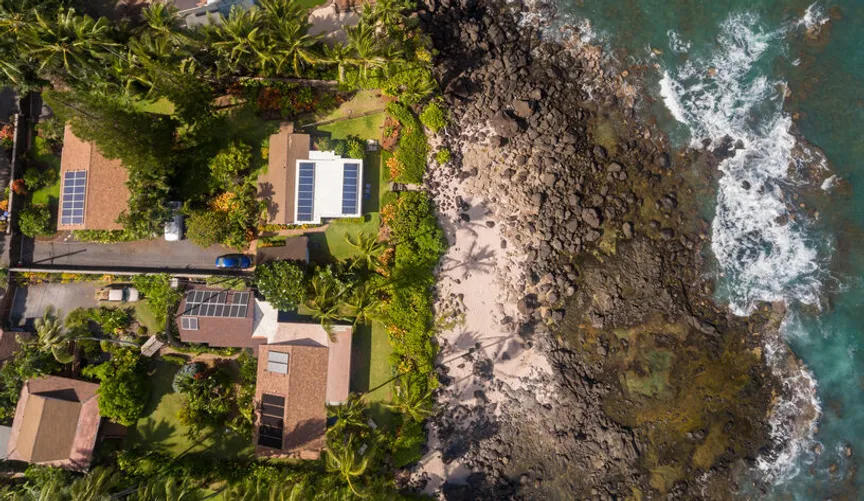 High-altitude view of the rugged Big Island shoreline at Ocean View, highlighting sustainable homes equipped with solar energy systems near the beach.