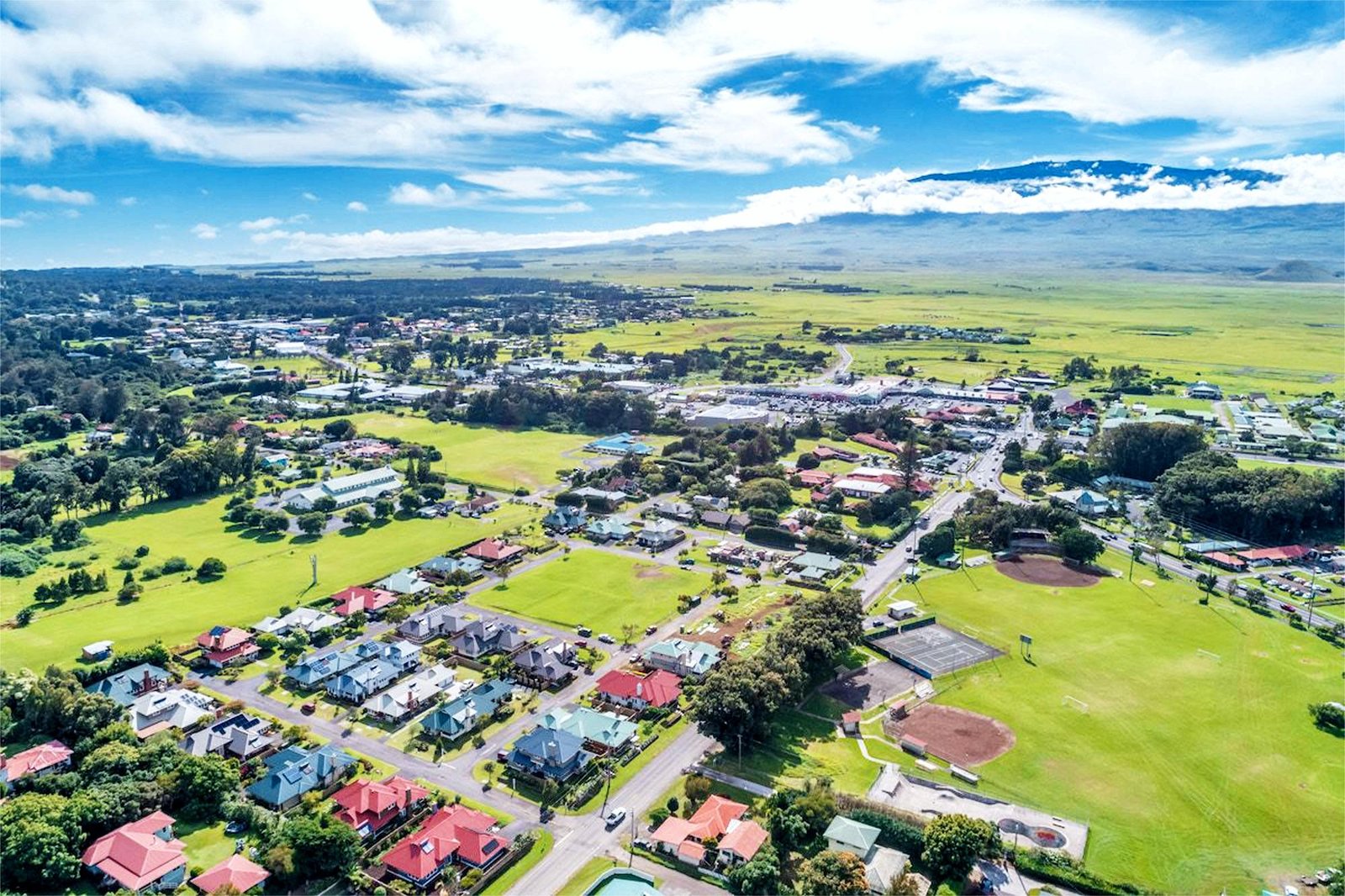 An aerial landscape view of the Waimea community in Hawaii, showing residential homes and green fields under a bright blue sky, ideal for solar installation.