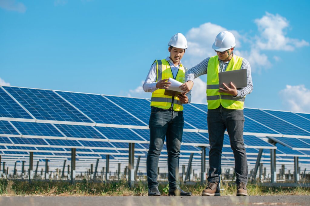 A diverse team of business executives standing proudly in front of a solar energy monitor and commercial solar panels, representing corporate sustainability.
