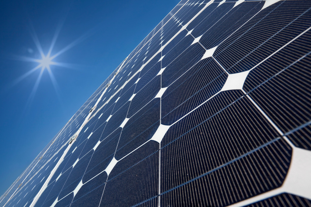 A detailed, low-angle close-up of high-efficiency monocrystalline solar panels under a bright, clear sky with a sunburst effect, representing durable energy solutions for Big Island businesses.