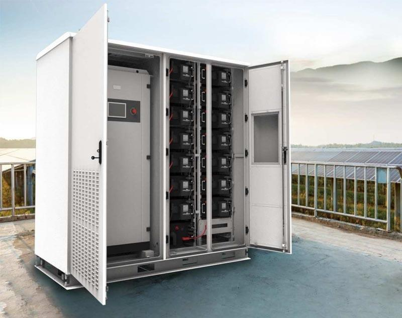 commercial battery storage unit with its white doors open, revealing rows of black battery modules and internal circuitry, installed on a rooftop next to solar panels in Hawaii to provide energy backup and grid resilience.
