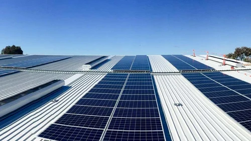 A wide view of a modern government complex or municipal building on the Big Island featuring a large, slanted standing-seam metal roof completely covered in rows of efficient blue solar panels under a clear sky.