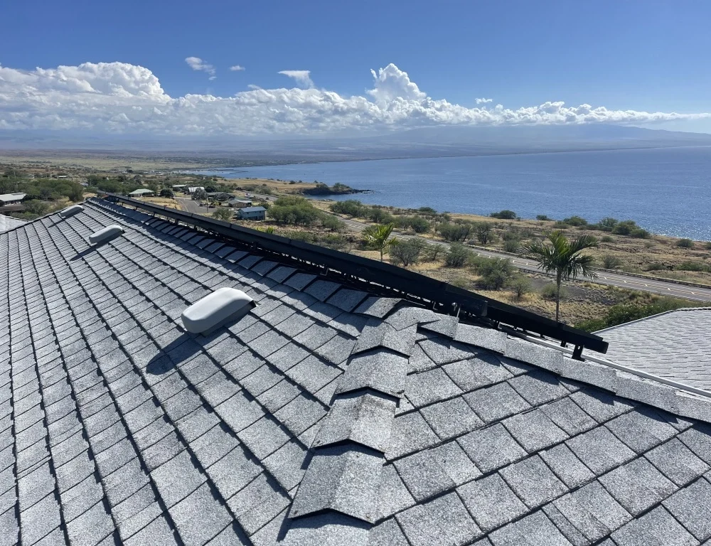 Residential rooftop solar panels installed on a shingle roof with a coastal landscape in the background.